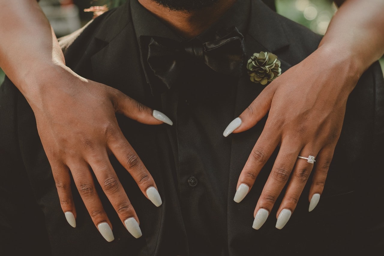 Woman with long fingernails and a dazzling princess cut ring embracing a man from behind