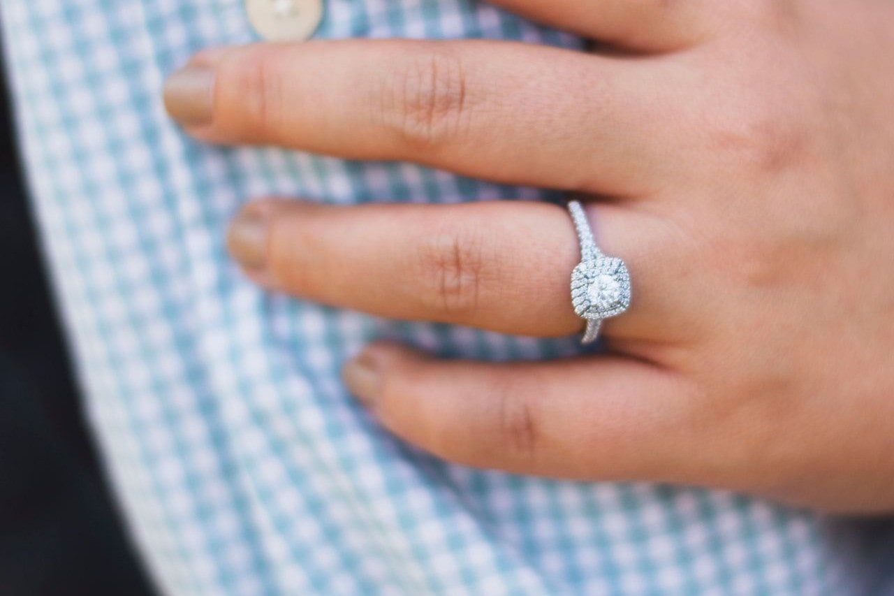 Woman showing off engagement ring with cushion cut diamond in a halo setting