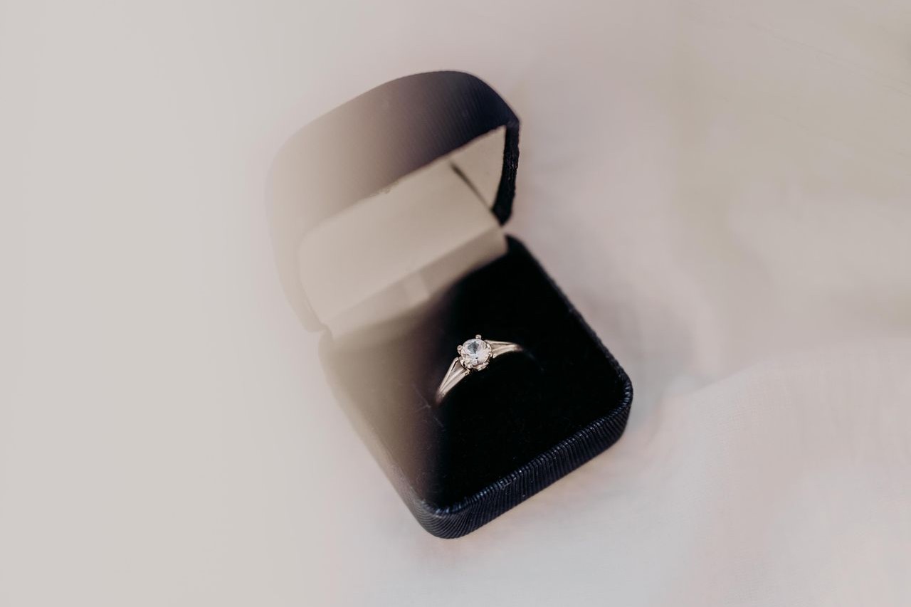 A solitaire diamond engagement ring in a black ring box on a white background