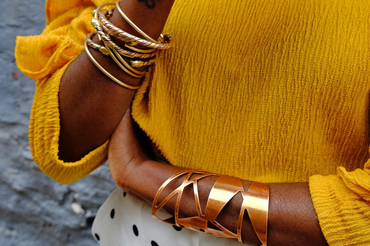 A woman with arms crossed wearing a variety of gold bangles and cuffs