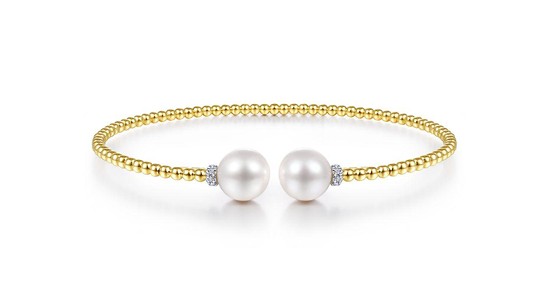 A gold cuff bracelet with a textured band and two pearls