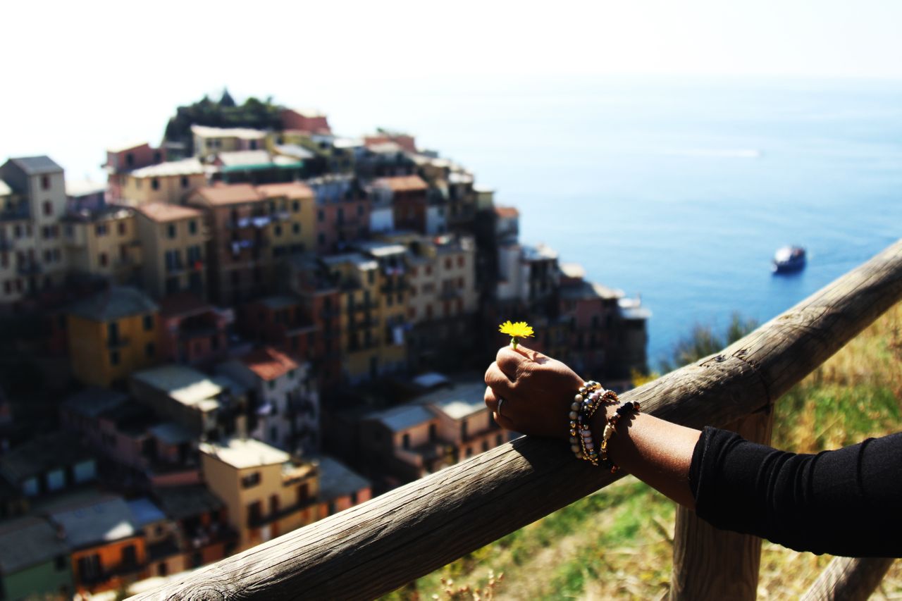 A woman’s arm resting on a wooden fence wearing a number of beaded bracelets and overlooking a city