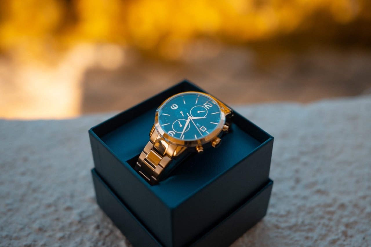A newly-purchased timepiece sits in a black box on a concrete bench during a fall day
