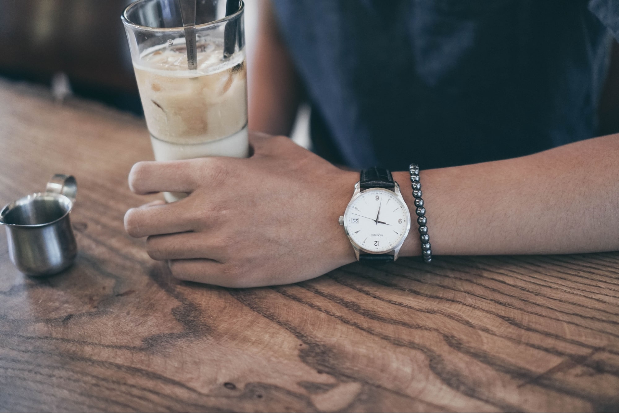 A man wearing a watch with a leather band sips his iced coffee at a diner
