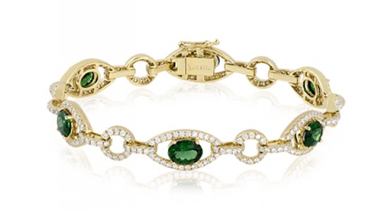 A yellow gold chain bracelet with green gems and diamond accents