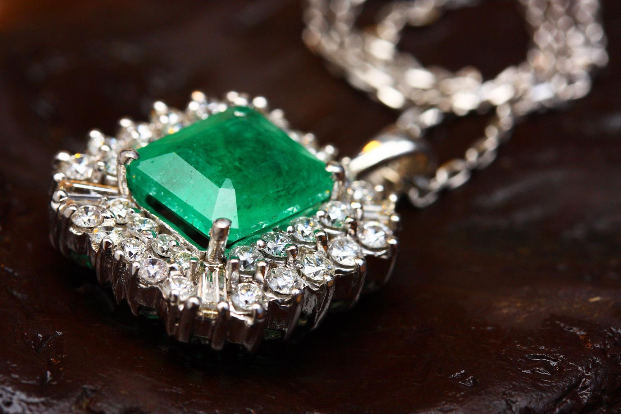 A bright green gemstone necklace surrounded by diamond accents