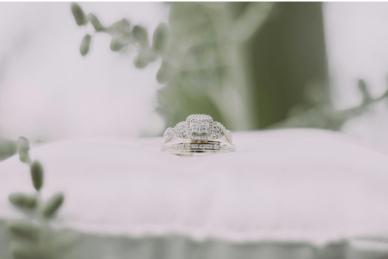 A modern halo white gold engagement ring sits on a ring pillow with a band.