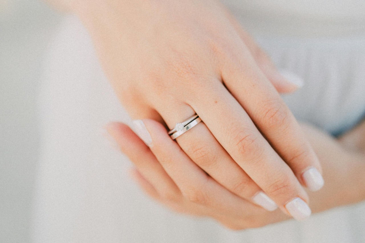 A woman wears a platinum solitaire engagement ring and wedding band.