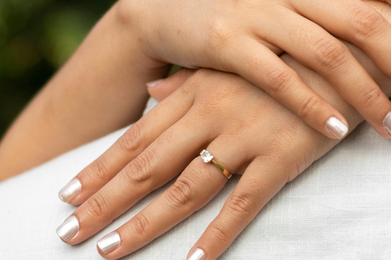 a woman hugging her partner wears a solitaire yellow gold ring.