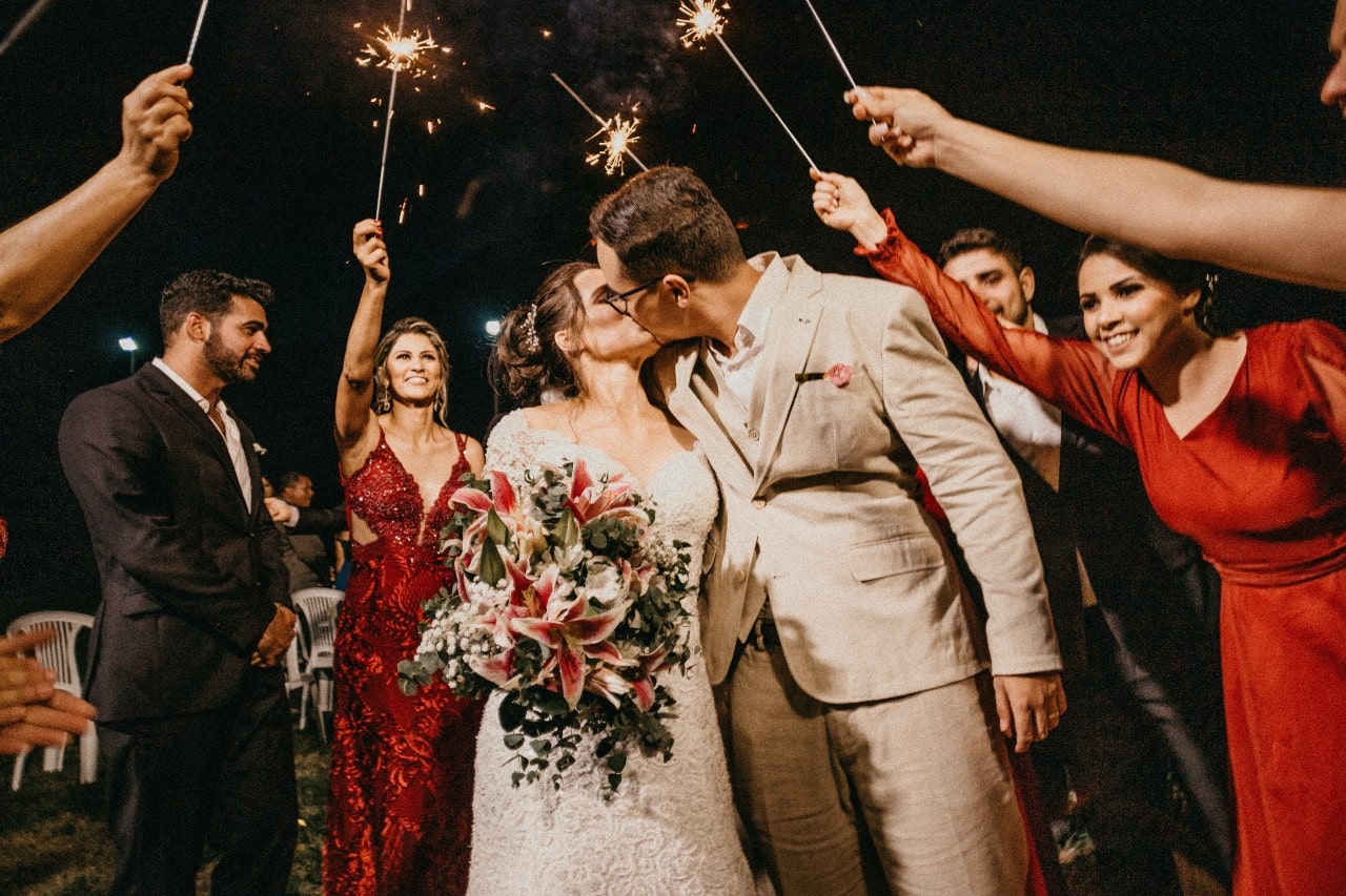 A bride and groom kissing during a night wedding, underneath festive sparklers.