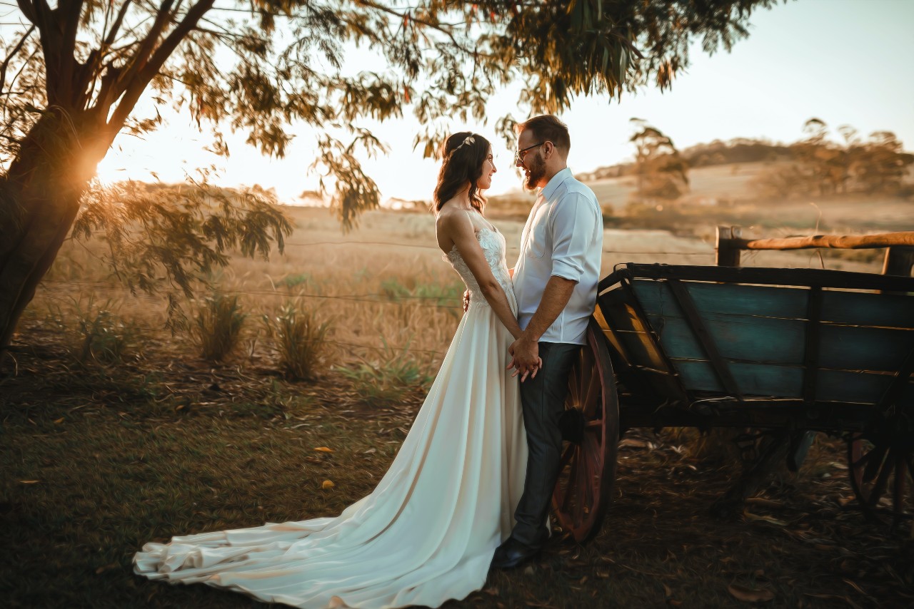 A photo of a minimalist bride and groom standing next to an old cart as the sun sets.