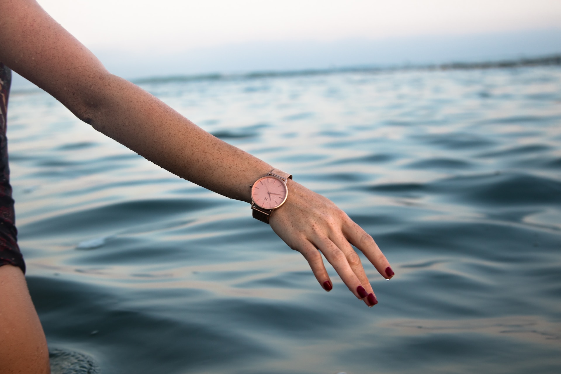 A close-up of a woman’s arm wearing a luxury watch as she prepares to swim in a lake.