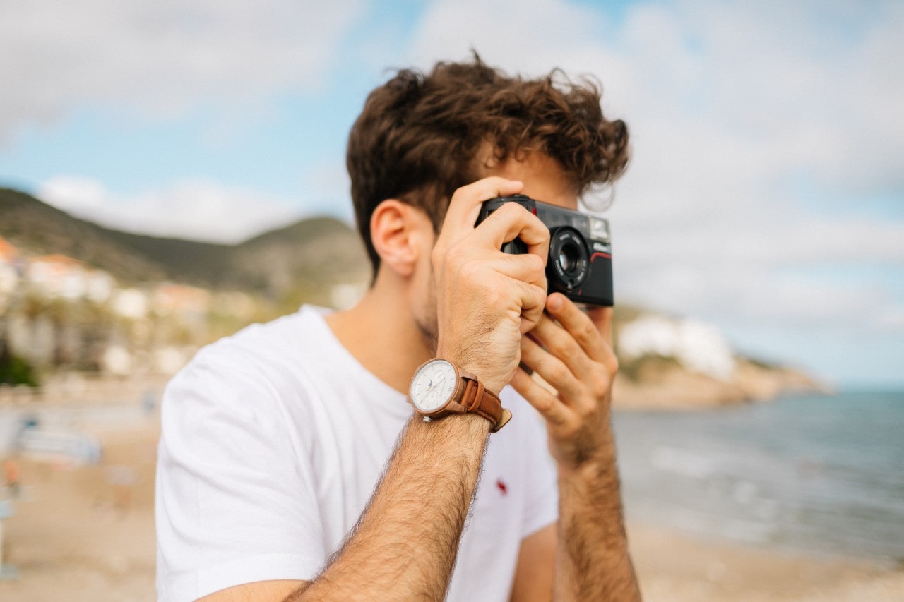 A young man wearing a luxury watch taking pictures at the beach.