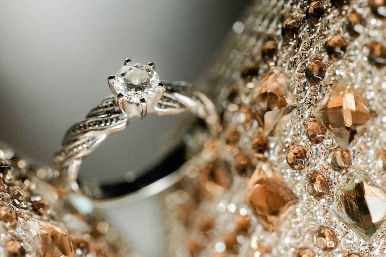 An engagement ring sits between two champagne-colored bedazzled surfaces.