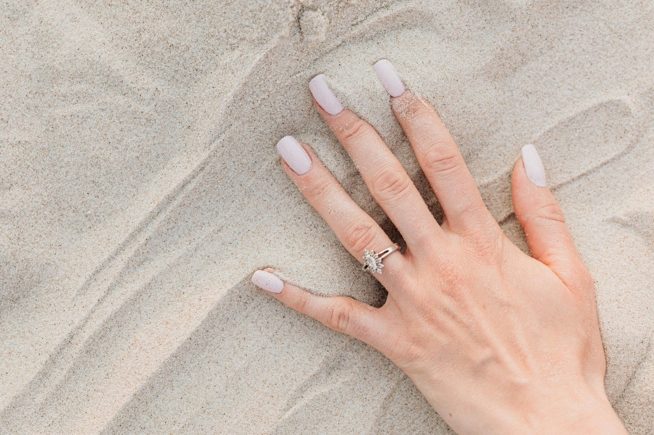 a woman’s hand in the sand, wearing a unique marquise cut engagement ring