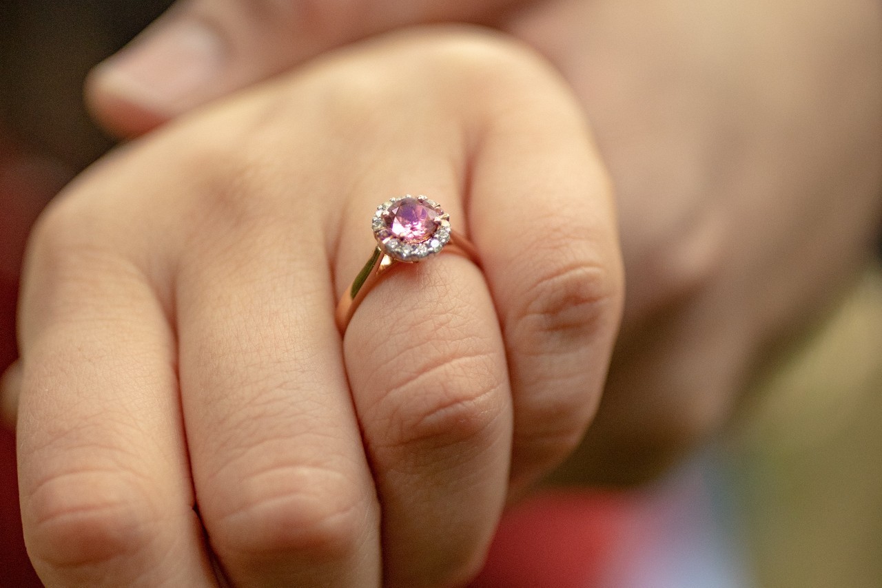 a woman’s hand wearing a rose gold engagement ring with a purple center stone