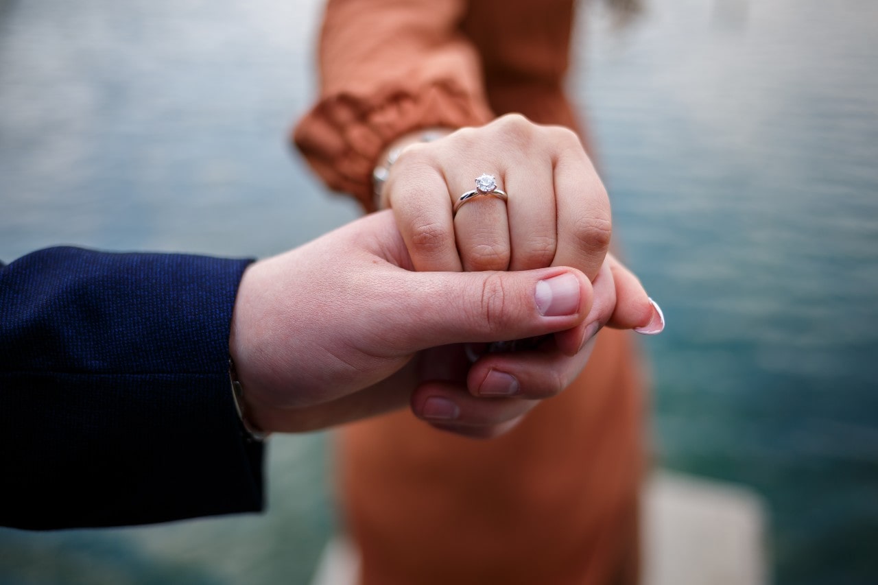 a man holding a woman’s hand wearing a solitaire engagement ring